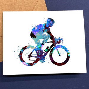 May include: A watercolor illustration of a cyclist on a bicycle. The cyclist and bike are rendered in shades of blue, purple, and red, with a splatter effect. The image is on a white card, with a brown envelope in the background.