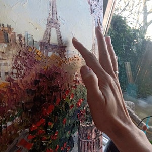 Può includere: Un dipinto della Torre Eiffel a Parigi, Francia. Il dipinto è realizzato in uno stile testurizzato con pennellate spesse. La Torre Eiffel è dipinta in tonalità di marrone e grigio, e lo sfondo è un cielo azzurro chiaro. Ci sono fiori rossi in primo piano.