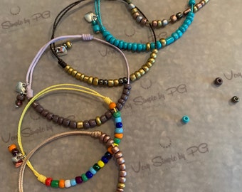May include: Five bracelets with different colored beads and charms. The bracelets are made with brown, gold, turquoise, and pink beads. The charms are silver hearts. The bracelets are on a white surface with the text "Very Simple by PG" printed on it.