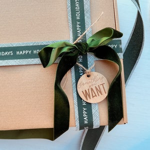 May include: A brown gift box wrapped in green and white striped ribbon with a green velvet bow. A wooden gift tag with the text "Something you WANT" is attached to the bow.