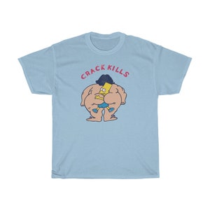 May include: Light blue t-shirt featuring a cartoon image of a yellow character with black hair and a blue shirt. The character is being hugged from behind by a larger, nude character with a yellow body. The text "CRACK KILLS" is printed in pink above the characters.