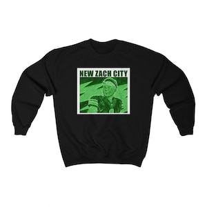 以下が含まれることがあります： 緑色のグラフィックでフットボール選手と「NEW ZACH CITY」の文字が書かれた黒いスウェットシャツです。