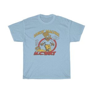 May include: Light blue t-shirt featuring a cartoon image of Bart Simpson as a rapper. The image includes the text "Dancin' Machine" and "MC. Bart".