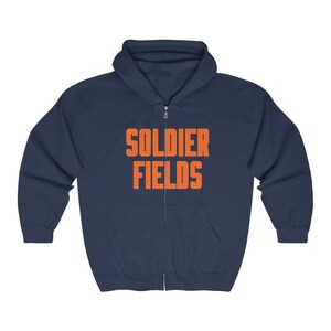 Könnte beinhalten: Ein marineblauer Kapuzenpullover mit Reißverschluss und dem Text "SOLDIER FIELDS" in Orange.