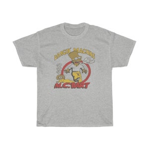 May include: A grey t-shirt featuring a cartoon image of Bart Simpson as a rapper. The text "Dancin' Machine" and "M.C. Bart" are printed on the shirt. The cartoon Bart Simpson is wearing a yellow shirt, blue jeans, and a backwards baseball cap. He is holding a microphone and has a surprised expression on his face. The text "You can't touch this!" is printed in a speech bubble above Bart Simpson's head.