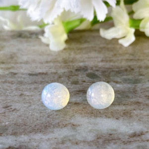 May include: A pair of iridescent opal stud earrings. The earrings are round and have a white and blue colour.