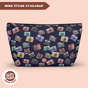 May include: A navy blue zippered pouch with a repeating pattern of colorful vintage cameras. The pouch is made of a soft, durable fabric and is perfect for storing small items like makeup, toiletries, or electronics.