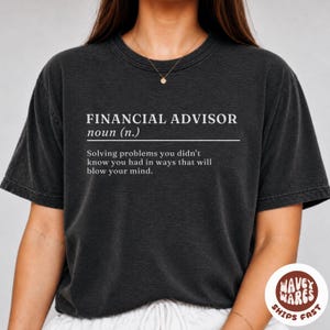 May include: A charcoal grey short-sleeve t-shirt featuring white text that reads: FINANCIAL ADVISOR noun (n.) Solving problems you didn't know you had in ways that will blow your mind. The shirt has a crew neckline and a vintage-style washed finish.