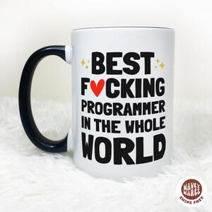 May include: White ceramic mug with a black handle and rim. The mug features the text "BEST FUCKING PROGRAMMER IN THE WHOLE WORLD" in black, with a red heart replacing the "O" in "FUCKING".