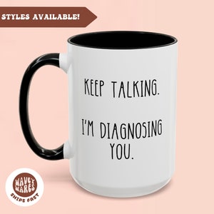 May include: White ceramic mug with a black handle and black rim. The mug has black text that reads "KEEP TALKING. I'M DIAGNOSING YOU."