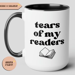 Może przedstawiać: Biały kubek ceramiczny z czarnym uchwytem i rantem. Kubek ma czarny napis "tears of my readers" ze stylizowanym obrazkiem otwartej książki pod tekstem.