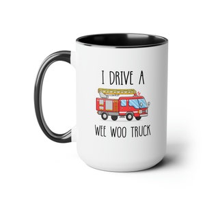 May include: White ceramic coffee mug with a black rim and handle. The mug has a cartoon image of a red fire truck with a ladder and the text "I drive a wee woo truck".
