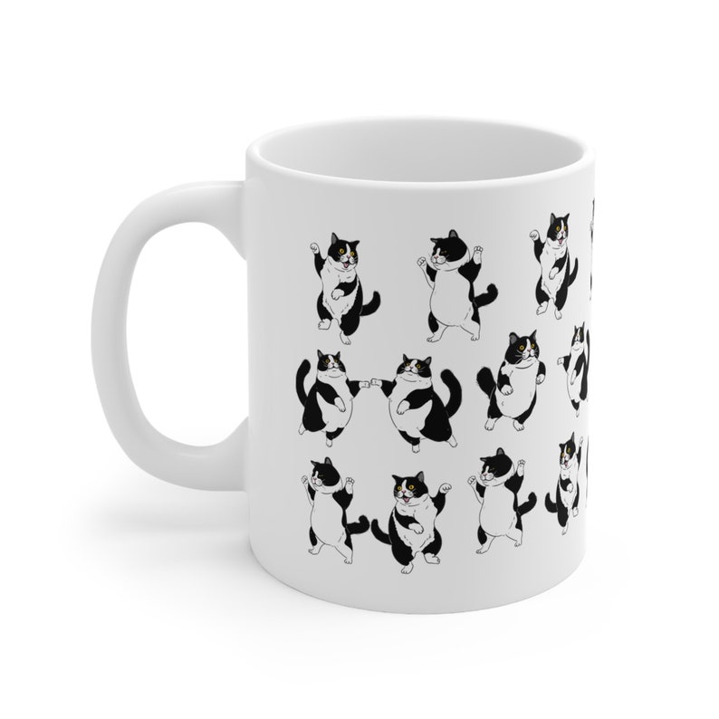 May include: White ceramic mug featuring a repeating pattern of cartoon tuxedo cats in various poses. The cats are black and white with yellow eyes. The mug has a white handle and a glossy finish.