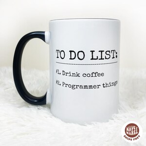 May include: White ceramic mug with a black handle. The mug features the text "TO DO LIST: #1. Drink coffee #2. Programmer things" in black. The mug has a glossy finish and is suitable for hot or cold beverages.