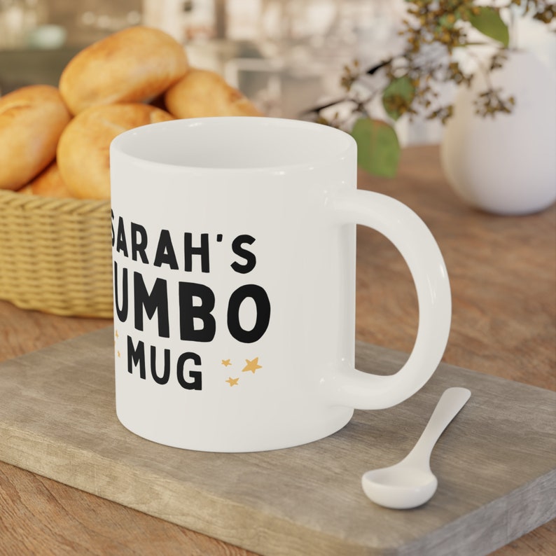 Może przedstawiać: Biały kubek ceramiczny z czarnym napisem "Sarah's Jumbo Mug" i złotymi gwiazdkami.