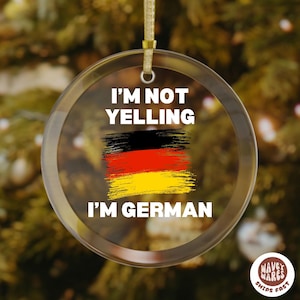 May include: Clear, round Christmas ornament with the text "I'M NOT YELLING I'M GERMAN" in white. The ornament features a painted German flag in black, red, and yellow. A gold-colored string is attached for hanging.
