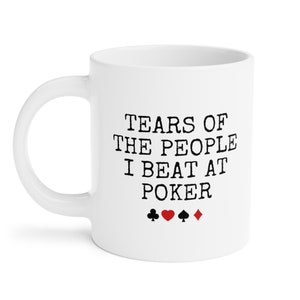 Puede incluir: Taza de caf&eacute; de cer&aacute;mica blanca con texto negro que dice "Tears of the people I beat at poker" y cuatro s&iacute;mbolos de palo de cartas negras: una pica, un coraz&oacute;n, un tr&eacute;bol y un diamante.