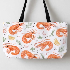 May include: A white tote bag with black shoulder straps featuring a repeating watercolour print of orange shrimp, yellow lemon slices, green herbs, garlic cloves, and black peppercorns scattered across the entire surface of the bag.