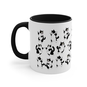 May include: White ceramic mug with a black handle and interior. The mug features a repeating pattern of cartoon tuxedo cats in various poses. The cats are black and white, with some having one yellow eye.