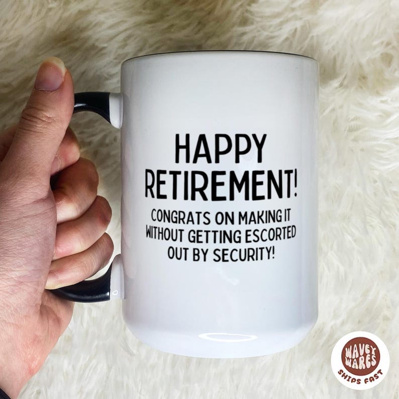 K&ouml;nnte beinhalten: Wei&szlig;er Keramikbecher mit schwarzem Henkel und Rand. Der Becher tr&auml;gt den Text "HAPPY RETIREMENT!" und eine humorvolle Botschaft &uuml;ber den Ruhestand. Eine Hand h&auml;lt den Becher.