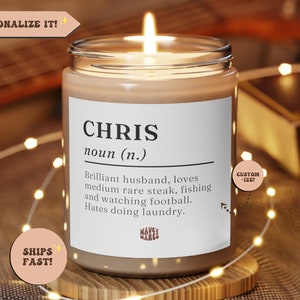Puede incluir: Una vela encendida en un tarro de cristal con una etiqueta blanca. La etiqueta dice "CHRIS" con una definición, incluyendo "ama el bistec poco hecho, la pesca y ver fútbol". La vela está rodeada de luces de hadas.