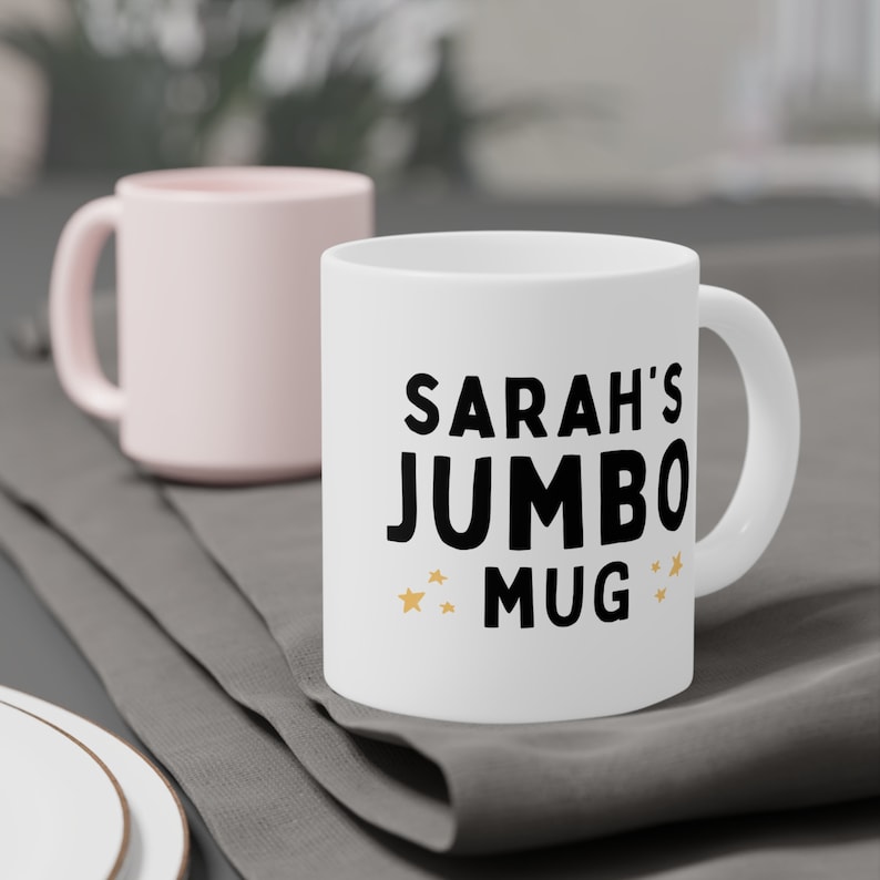 Może przedstawiać: Biały kubek ceramiczny z czarnym tekstem, kt&oacute;ry brzmi "Sarah's Jumbo Mug" ze złotymi gwiazdkami po obu stronach tekstu.