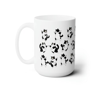 May include: White ceramic mug featuring a repeating pattern of cartoon tuxedo cats in various poses. The cats are black and white with yellow eyes. The mug has a large handle and a smooth, glossy finish.