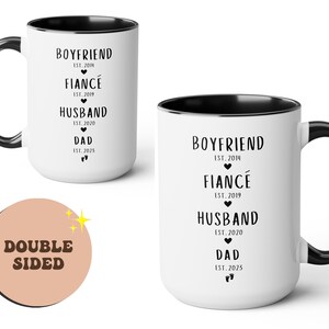 K&ouml;nnte beinhalten: Eine wei&szlig;e Keramik-Kaffeetasse mit schwarzem Rand und Henkel. Die Tasse hat schwarzen Text mit der Aufschrift "Boyfriend Est. 2014, Fianc&eacute; Est. 2019, Husband Est. 2020, Dad Est. 2025". Die Tasse ist doppelseitig.