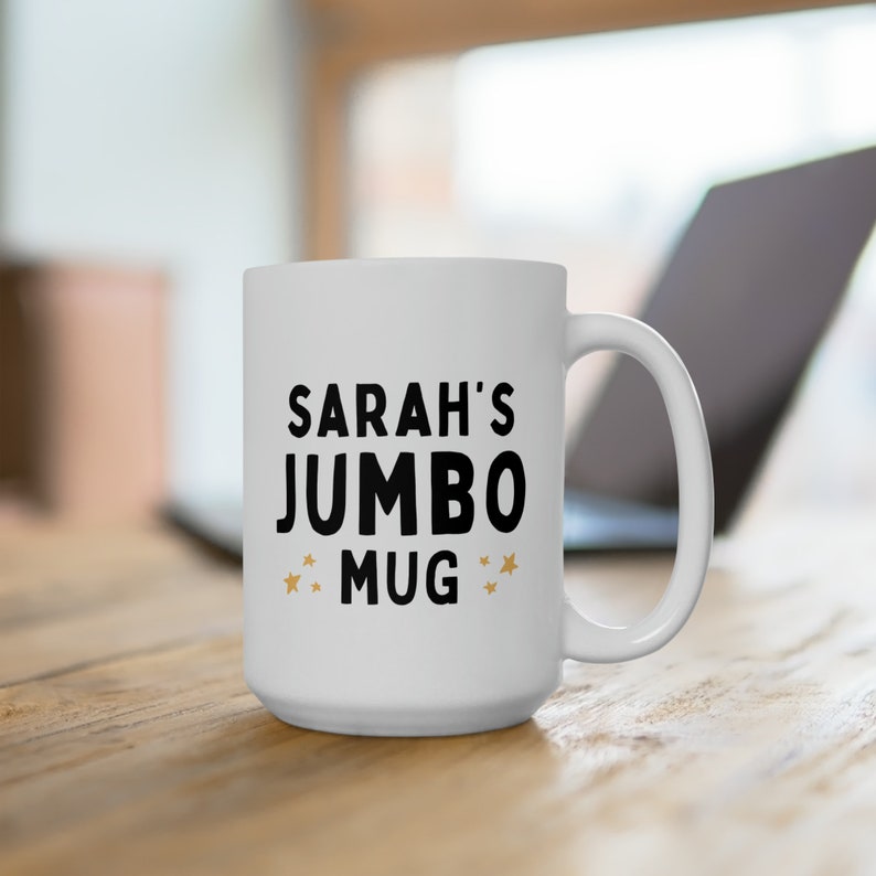 Może przedstawiać: Biały kubek ceramiczny z czarnym tekstem, kt&oacute;ry brzmi "SARAH'S JUMBO MUG" z dwiema złotymi gwiazdkami po obu stronach tekstu.