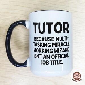 Op de afbeelding: Witte keramische mok met een zwart handvat en rand. De mok heeft het woord "TUTOR" in grote zwarte letters, gevolgd door een humoristische uitspraak over de functietitel. De mok heeft het "WAVEY WARES"-logo.