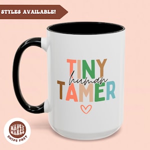 Peut inclure: Une tasse en céramique blanche avec une poignée noire. La tasse présente un motif coloré qui dit "Tiny human tamer" avec un petit cœur rose en bas.