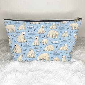 May include: A light blue zipped pouch featuring an all-over print of white polar bears in various poses, including sitting, walking, and lying down, interspersed with small illustrations of icebergs, snowflakes, and dark paw prints.