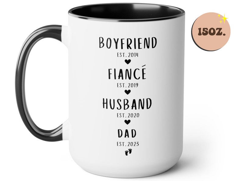 K&ouml;nnte beinhalten: Eine wei&szlig;e Keramiktasse mit schwarzem Rand und Henkel. Die Tasse hat schwarzen Text, der "Boyfriend Est. 2014", "Fianc&eacute; Est. 2019", "Husband Est. 2020" und "Dad Est. 2023" lautet. Die Tasse hat ein Fassungsverm&ouml;gen von 440 ml.