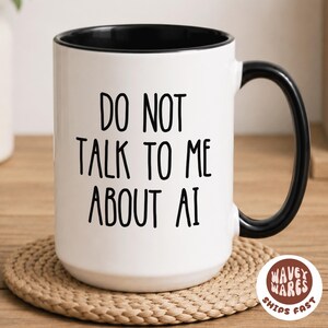 May include: White ceramic mug with a black interior and handle. The mug features the text "DO NOT TALK TO ME ABOUT AI" in black lettering. The mug is sitting on a woven coaster.