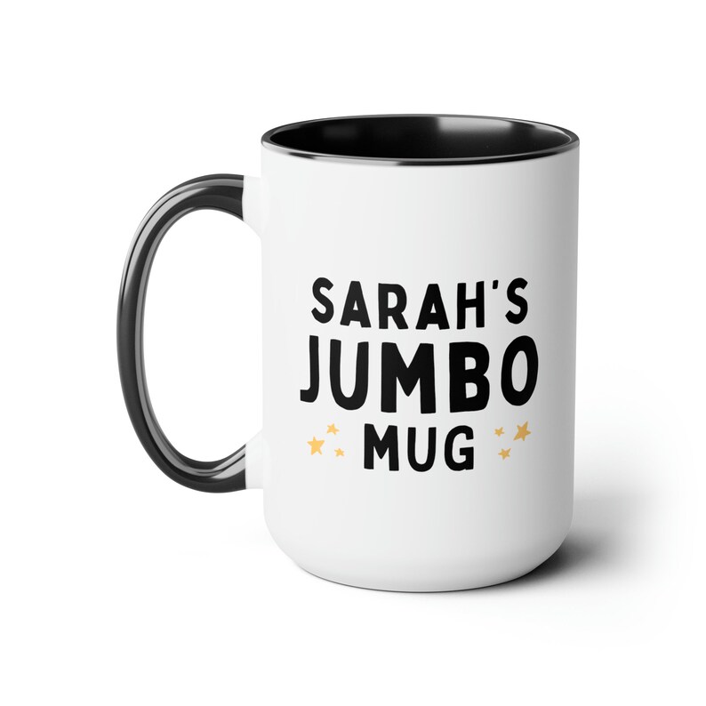 Może przedstawiać: Biały kubek ceramiczny z czarną obw&oacute;dką i uchwytem. Kubek ma czarny napis "SARAH'S JUMBO MUG" z małymi złotymi gwiazdkami po obu stronach napisu.