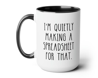 May include: White ceramic coffee mug with a black rim and handle. The mug has black text that reads "I'm quietly making a spreadsheet for that."