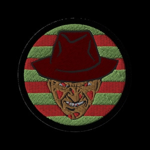 Puede incluir: Un parche circular de rayas rojas y verdes con una máscara de Freddy Krueger roja y negra en el centro. La máscara tiene un sombrero rojo de ala ancha y una expresión aterradora.