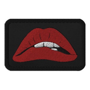 May include: A red embroidered patch with a pair of lips biting the lower lip. The patch is on a black background.
