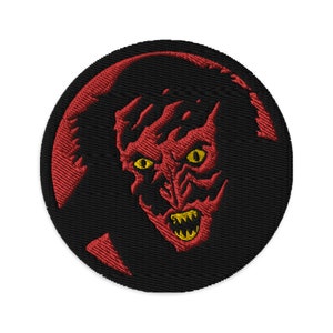 May include: Red and black embroidered patch featuring a demonic face with yellow eyes and sharp teeth. The face is surrounded by a black circle with a red crescent moon shape.