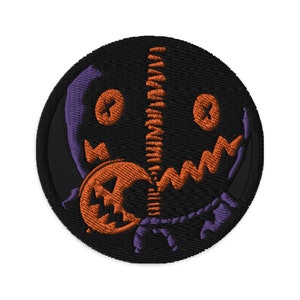 May include: Embroidered patch featuring a black and purple stitched face with a stitched-on orange pumpkin. The pumpkin has a stitched-on face with a wide grin and two eyes.