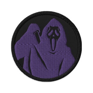 May include: Embroidered patch featuring a purple Scream mask design on a black circular background. The patch has a black border and is made of fabric. The design is a stylized representation of the iconic horror movie character.
