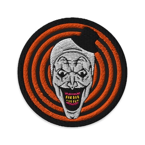 Può includere: Toppa ricamata con un clown inquietante con un ampio sorriso pieno di denti. Il viso del clown è bianco con occhi neri e una bocca rossa. La toppa è su uno sfondo nero con cerchi concentrici arancioni.