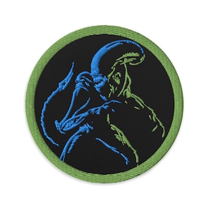 May include: A green and blue embroidered patch featuring a silhouette of an alien creature on a black background.