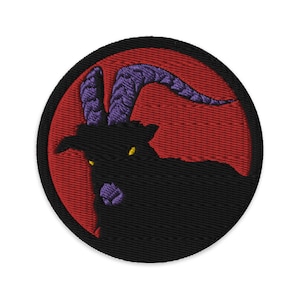 May include: Embroidered patch featuring a black goat with purple horns against a red background. The goat has yellow eyes and is facing the left side of the image.