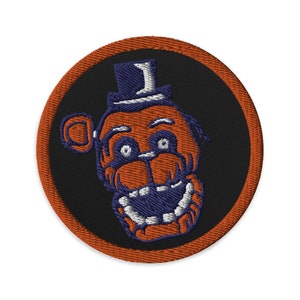 Peut inclure: Patch brodé orange et bleu d'un ours de dessin animé portant un haut-de-forme. L'ours a un large sourire et de grands yeux.