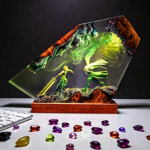 May include: A resin sculpture featuring two figures in a battle scene, encased in a clear, angled block. The base is wood, and the sculpture has a vibrant color palette with green, orange, and yellow hues. The base reads "Dandy's Crafts". Assorted colorful gems are scattered in front.