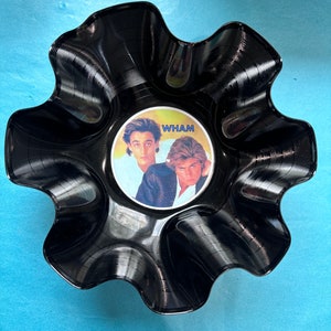 May include: A black vinyl record bowl with a scalloped edge. The bowl features a picture of the band Wham! on the front.