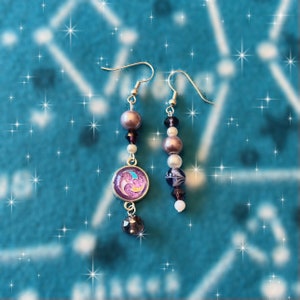 May include: A pair of dangle earrings featuring purple and white beads and a purple and pink charm. The charm has a swirl design.