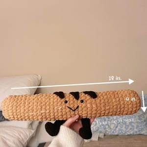 May include: A brown crocheted plush toy shaped like a corn cob with a smiling face. The toy is 18 inches long and 4 inches wide. The toy is labeled "Hours to Flowers".