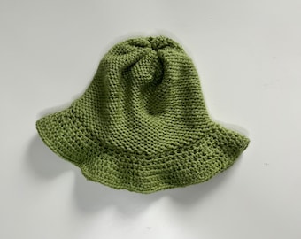 Puede incluir: Un sombrero de cubo de crochet verde.